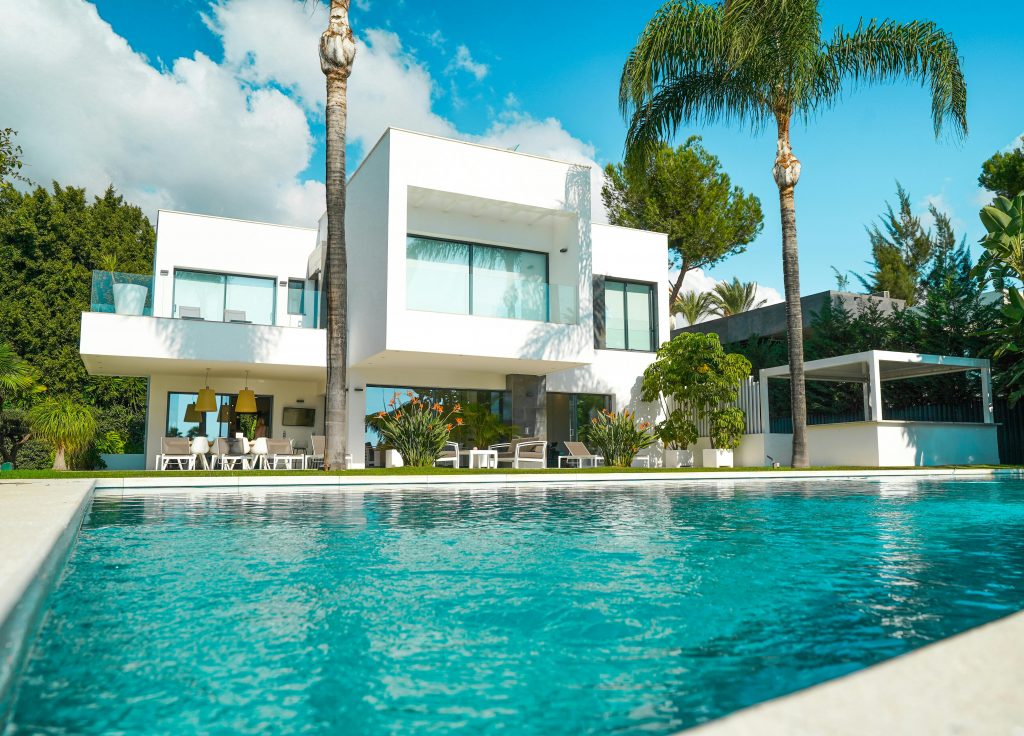 A stunning modern luxury villa with a pool, surrounded by lush greenery and bathed in sunlight.