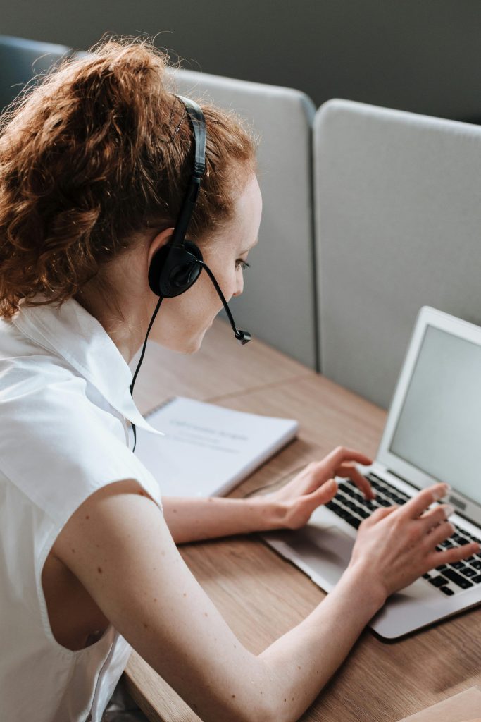 A woman working on a laptop with a headset in an office setting, focused on typing.